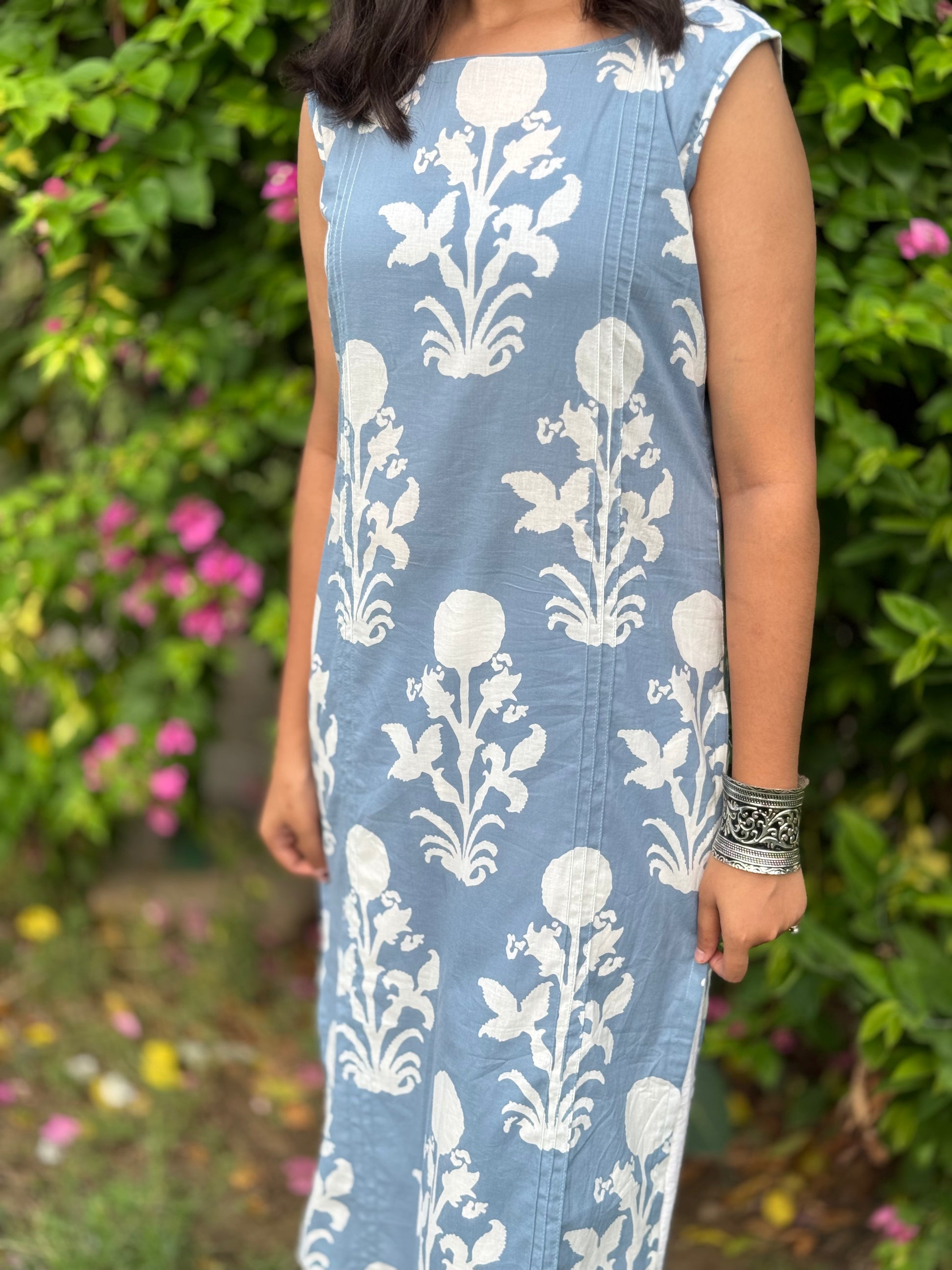 Person wearing a blue dress with white floral patterns in a garden setting