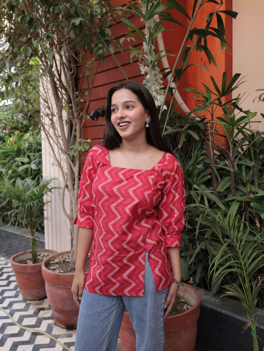 Woman in a red chevron-patterned dress standing outdoors with plants and a patterned floor.